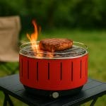 Barbecue da tavolo a carbone con carne in cottura e fiamma viva all’aperto
