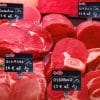 Cartellini segnaprezzi neri esposti su banco macelleria con tagli di carne fresca