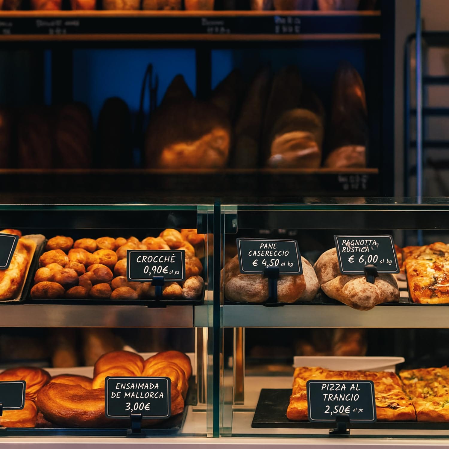 ambientata-kit-segnaprezzi-neutro Cartellini neri esposti su banco panificio con pane, pizza e prodotti da forno