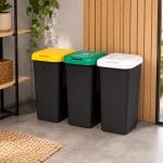 Pattumiera tripla con coperchi colorati per la casa Set di tre pattumiere nere con coperchi colorati bianco, verde e giallo collocate in un ambiente domestico