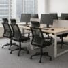Ufficio moderno con 4 sedie ergonomiche in rete nera davanti a scrivanie condivise con monitor e tastiere