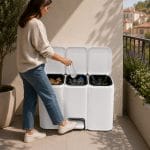 Pattumiera differenziata a pedale per balcone Donna che inserisce una bottiglia nella pattumiera differenziata bianca a tre scomparti usando il pedale