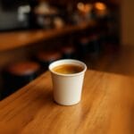 Bicchierino caffè in cartoncino bianco con espresso servito su tavolo di legno