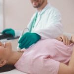 Medico utilizza gel conduttore per ecografia sul collo di una paziente