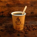Bicchierino caffè chicco con paletta in legno e chicchi ambientato su tavolo rustico
