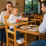 Bambino mangia al tavolo seduto su seggiolone in legno di faggio ciliegio con seduta in paglia